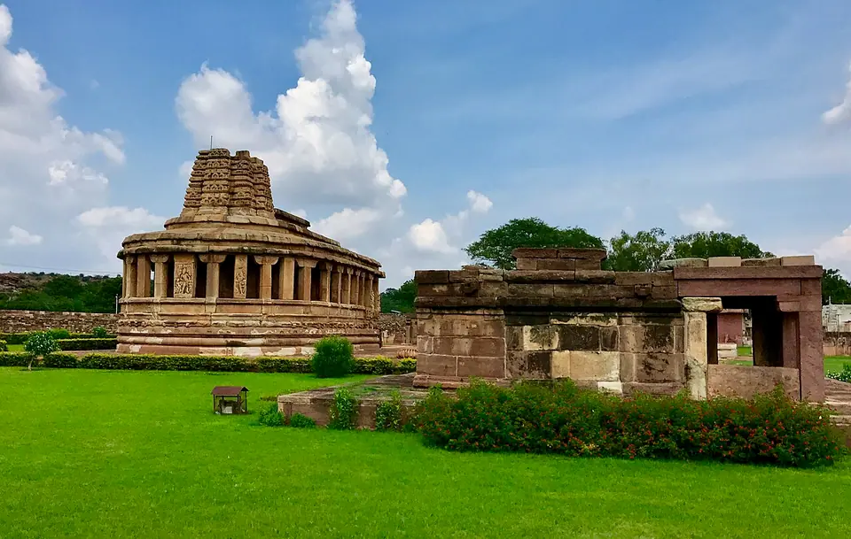 The apsidal stone Durga temple at Aihole, Karnataka, on a lawn beside smaller ruined shrines