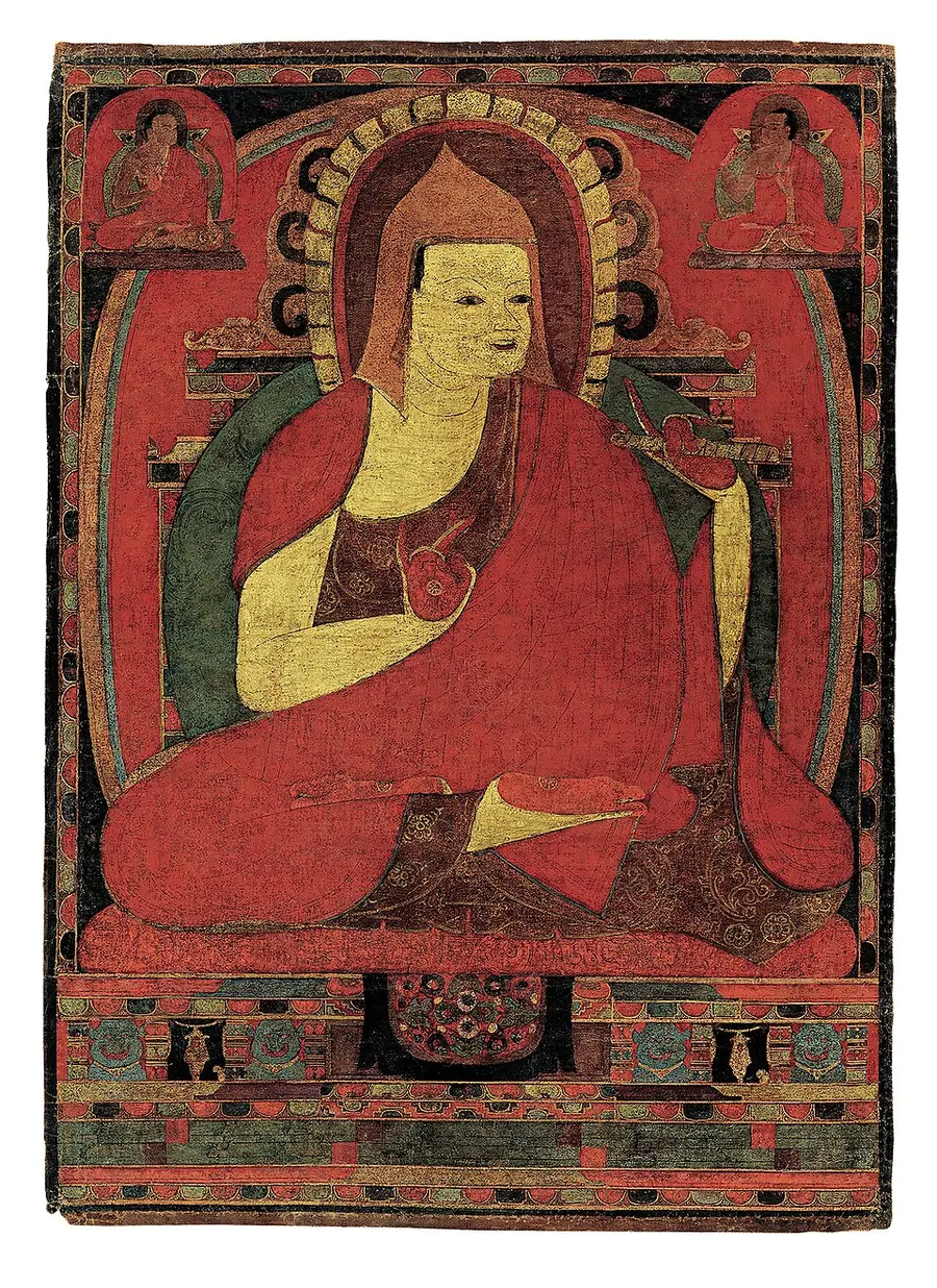 Tibetan painting of Atiśa seated cross-legged in red monastic robes and a pointed hat against a red background with two small teachers above