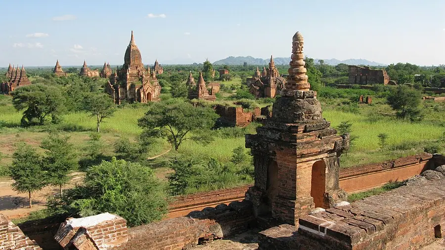 Brick temples and stupas of Old Bagan scattered across green fields, with hills on the horizon and a small shrine in the foreground