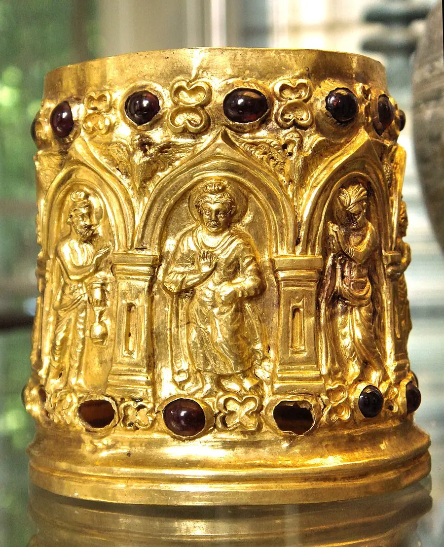 Small gold reliquary set with garnets, showing a standing Buddha with a halo between two attendants under arches