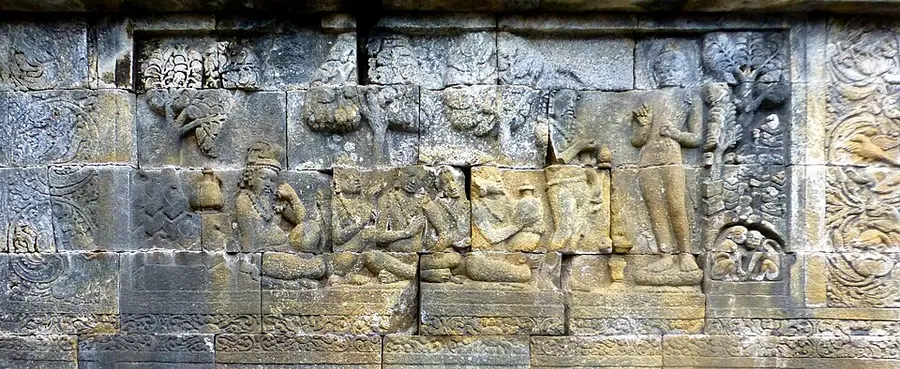 Weathered stone relief panel from Borobudur showing a standing figure at right facing a group of seated ascetics and attendants