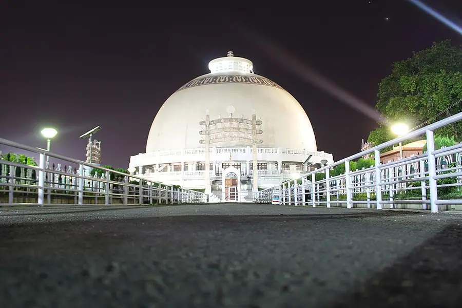 The white hemispherical stupa of Deekshabhoomi in Nagpur lit at night, approached along a railed walkway