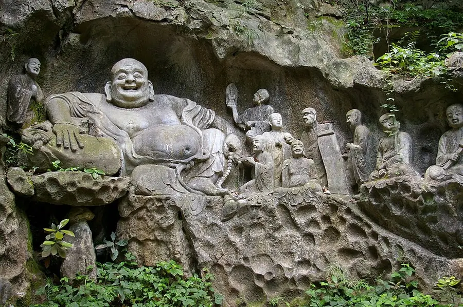A huge, laughing, pot-bellied Budai carved in grey rock at Feilaifeng, Hangzhou, with smaller carved arhats around him