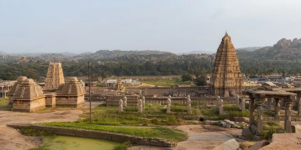 Temple ruins at Hampi with the tall gopuram of the Virupaksha temple and rocky hills behind