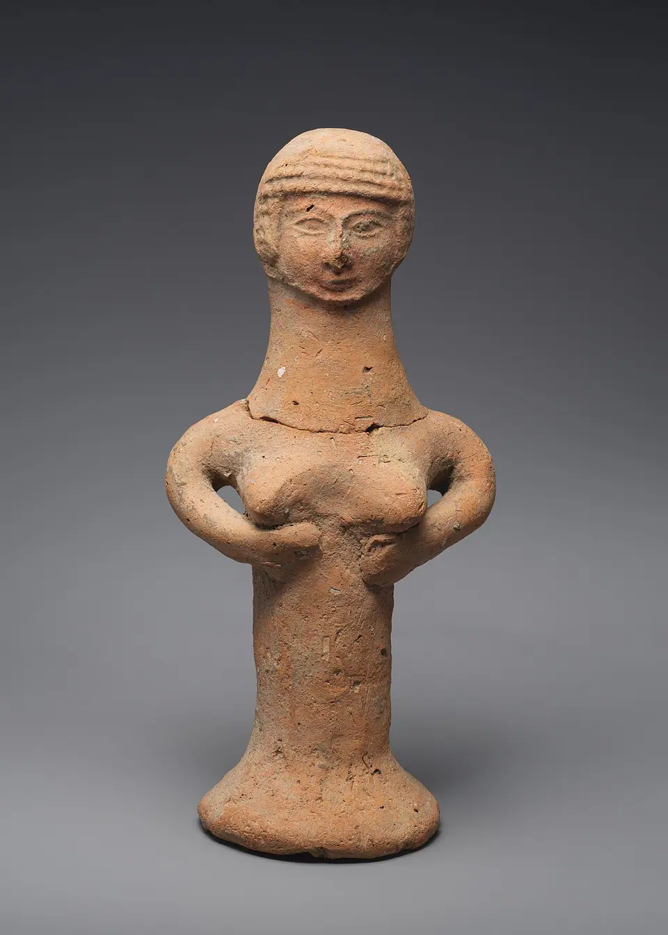 A small clay figurine of a woman with a pillar-shaped body, holding her breasts
