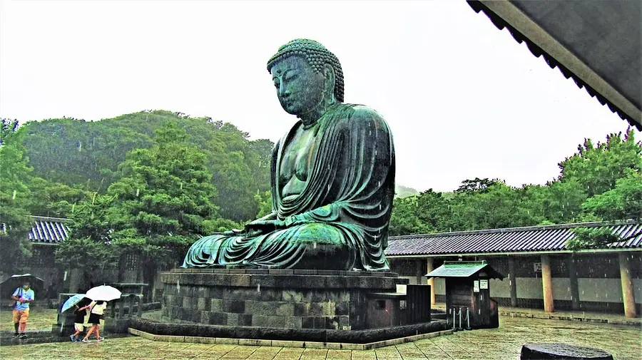 The bronze Great Buddha of Kamakura, a seated Amida Buddha green with age, on a stone platform in the open air, seen from the side in the rain