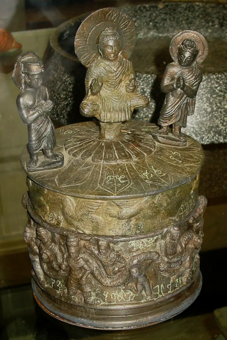Bronze cylindrical reliquary with a seated Buddha on the lid between two standing figures and a frieze with inscriptions round the sides; a replica of the Kaniṣka casket