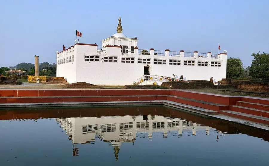 The white Maya Devi Temple at Lumbini reflected in the sacred pool, with Ashoka's pillar standing at the left
