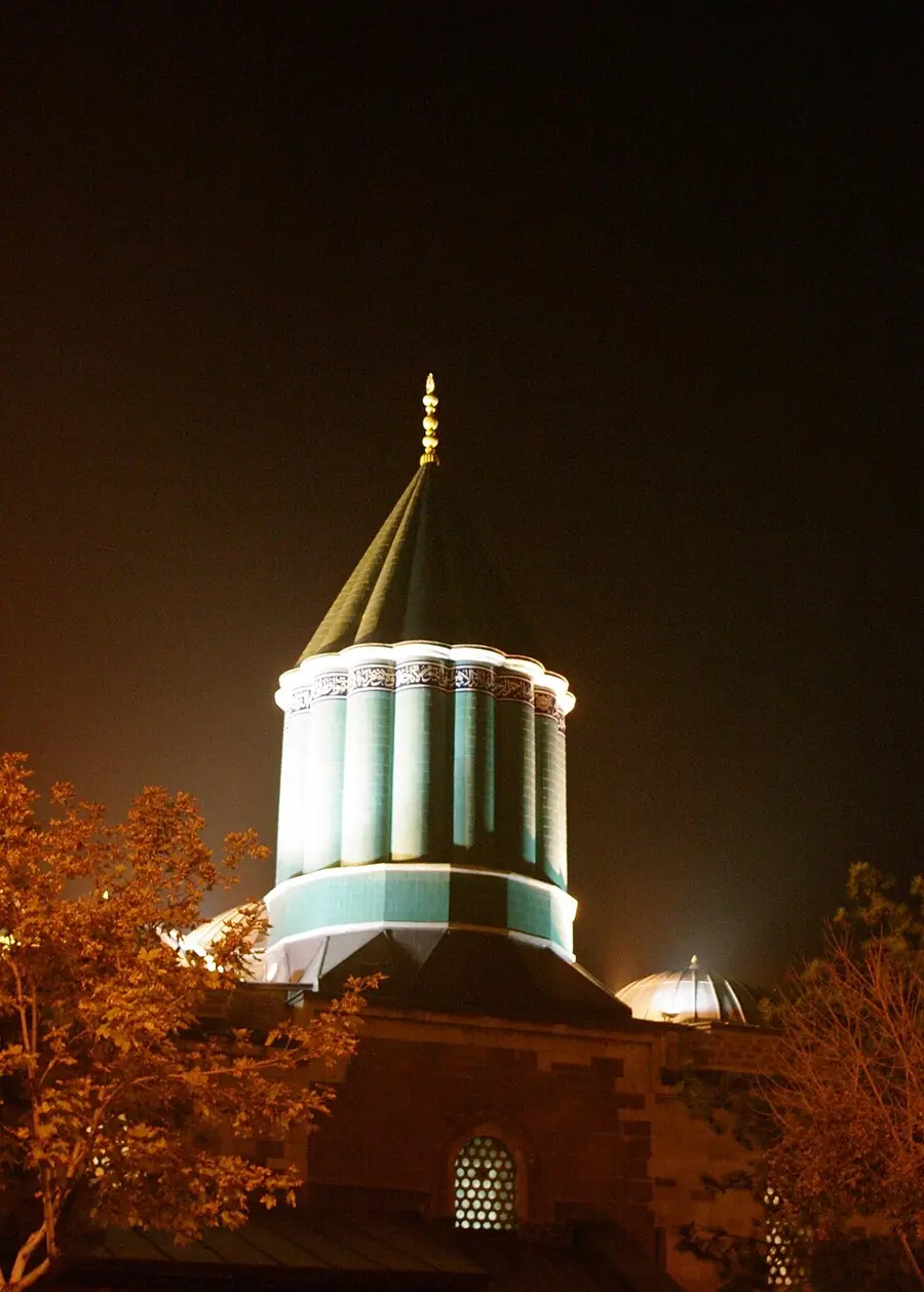 The fluted turquoise conical dome over Rūmī's tomb in Konya, lit at night