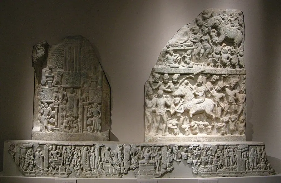 Three carved limestone relief panels from Nāgārjunakoṇḍa displayed in a museum, crowded with figures, a horse and a stupa