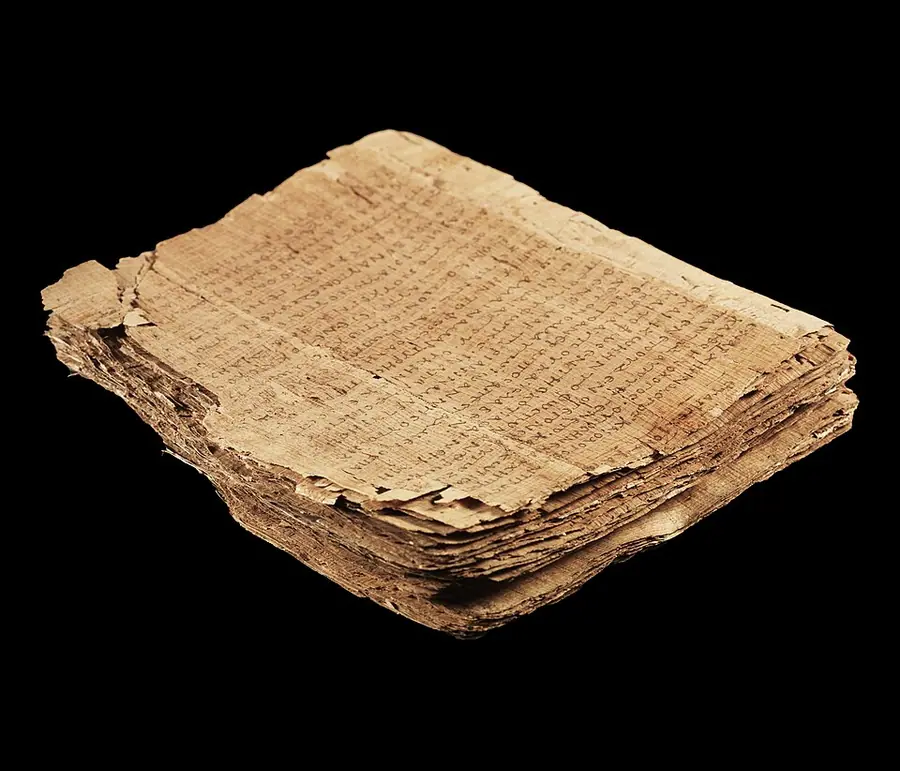 Papyrus 66, a thick stack of brown papyrus leaves of the Gospel of John written in Greek, photographed against black