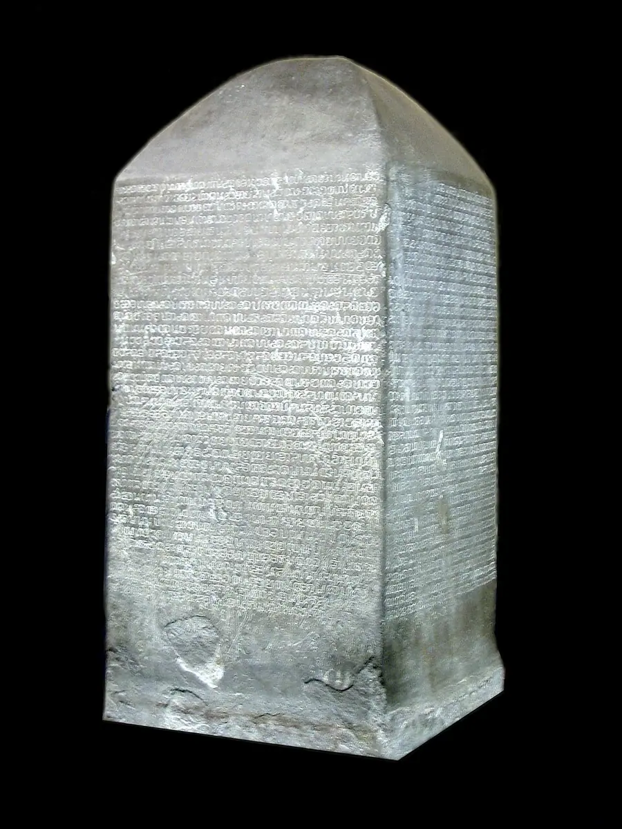 Four-sided grey stone stele with a pyramidal top, its faces covered in rows of early Thai script