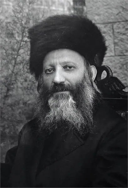 Head-and-shoulders photograph of Rabbi Abraham Isaac Kook in a tall fur hat, with a long grey-streaked beard, in front of a stone wall