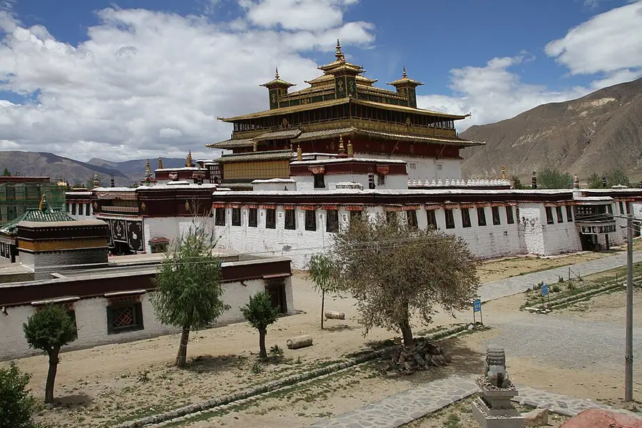 The main temple at Samye, a tiered building with gilded roofs rising above whitewashed monastery walls, with brown mountains behind