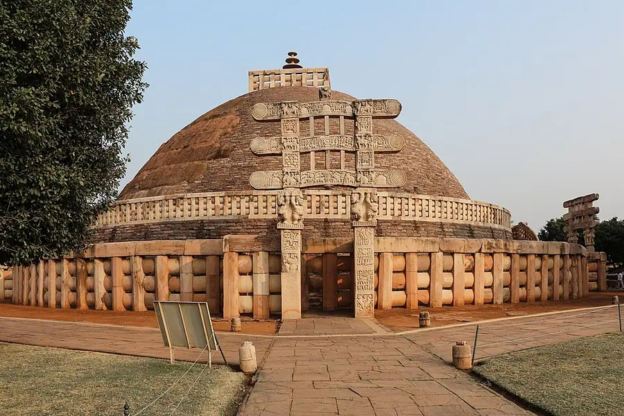 The Great Stupa at Sanchi, a broad hemispherical dome on a terrace, ringed by a stone railing with a carved gateway in front