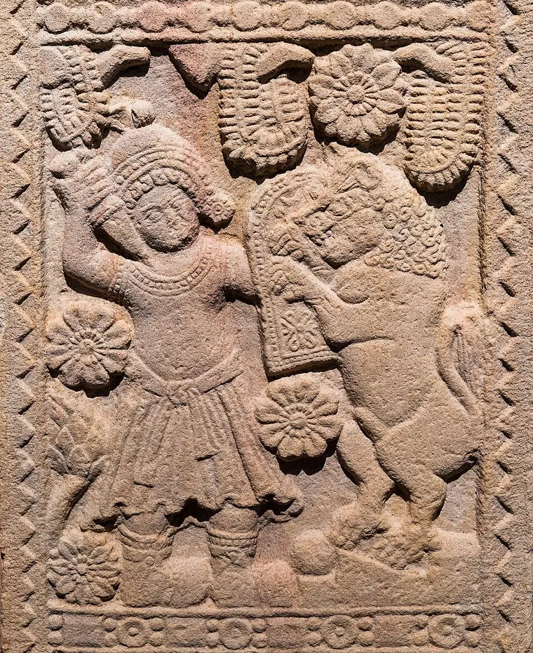 Carved sandstone railing relief from Sanchi Stupa 2 showing a figure beside a rearing animal, with rosettes
