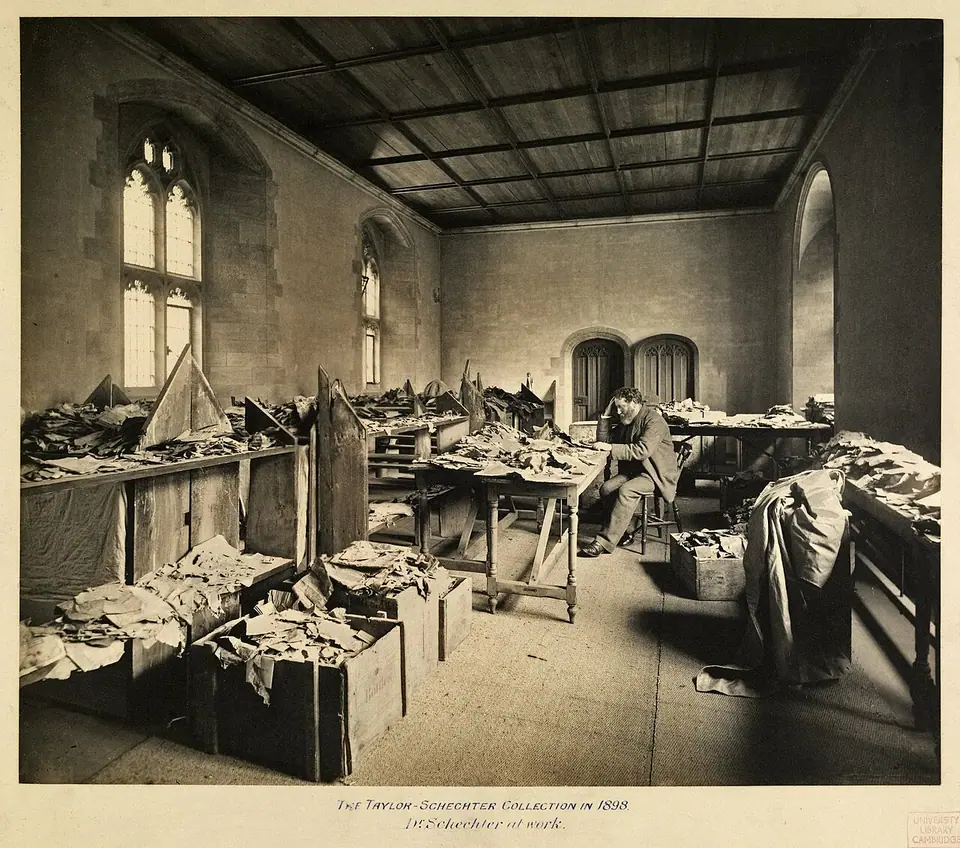 Solomon Schechter seated at a table in Cambridge University Library surrounded by boxes and piles of Genizah fragments