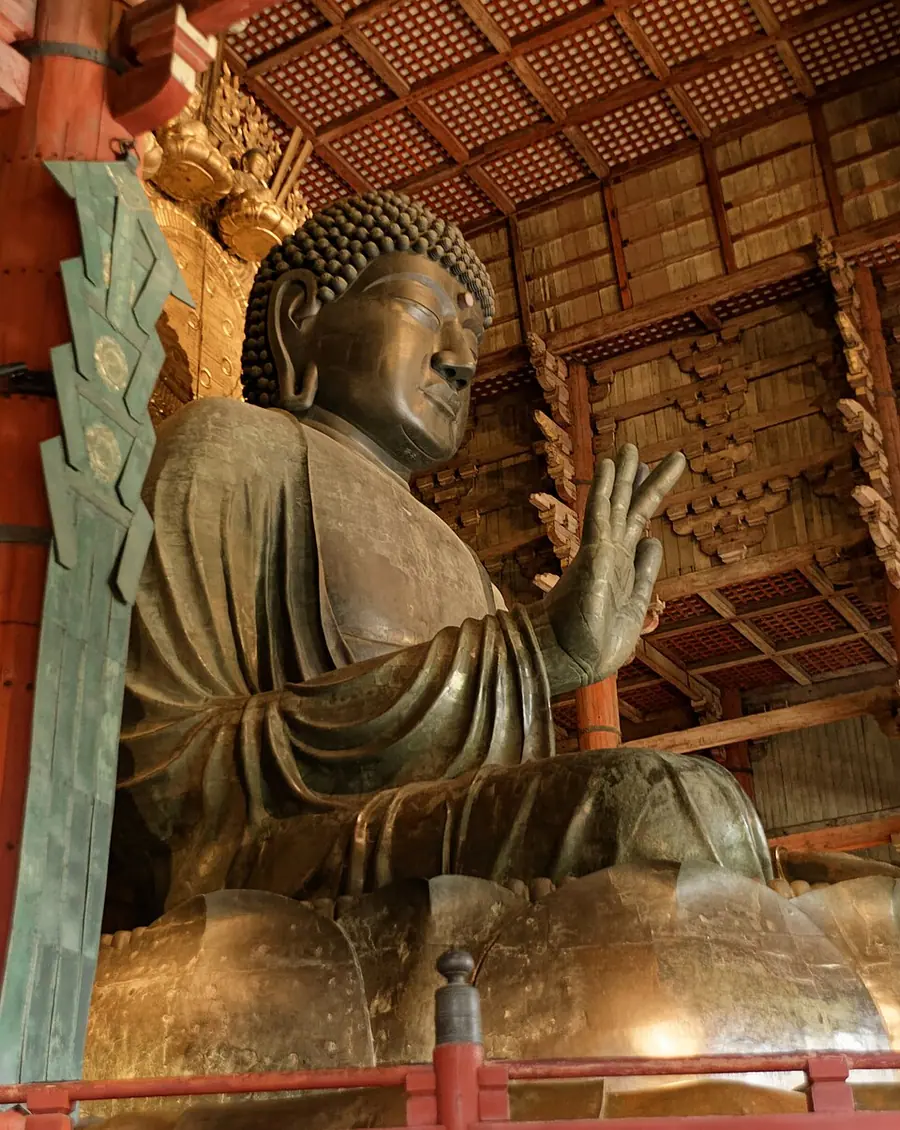 The colossal bronze seated Vairocana of Tōdaiji seen from below, right hand raised, under the wooden bracketing of the Great Buddha Hall